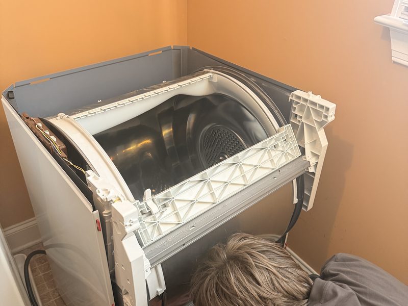 Appliance Priority Solutions technician working behind a dryer with the drum and front panel removed